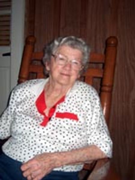 Elderly woman smiling warmly while sitting on a wooden chair.