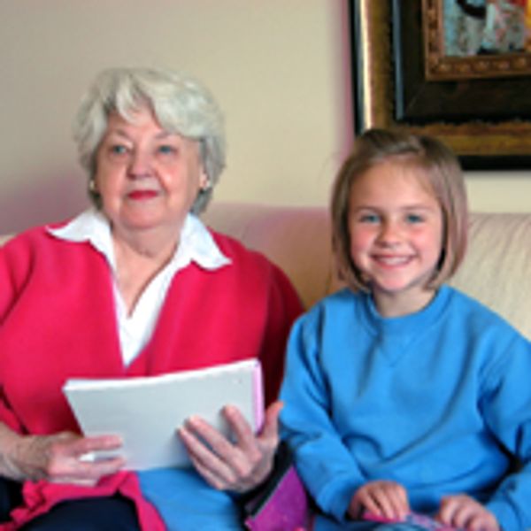 Elderly woman and young girl sitting together on a couch, smiling.