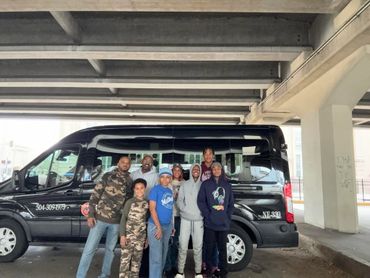 A group of people posing in front of a black van under a bridge.