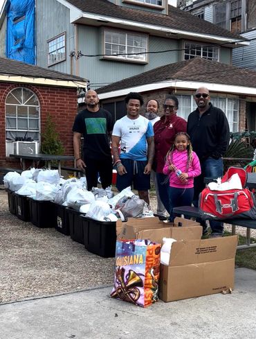 A group of people stand behind bins filled with packed goods outside a house.