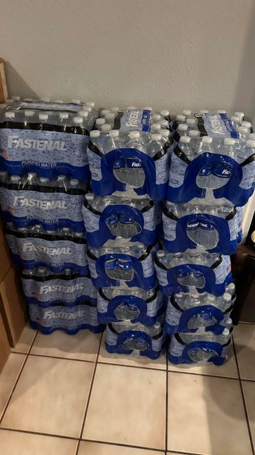 Stacks of Fastenal purified water bottles in a room corner.