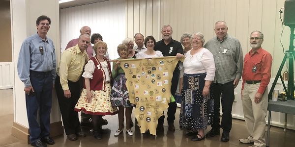A group of people holding a decorated yellow fabric in a community hall.