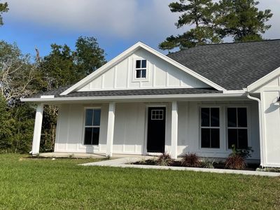 White modern farmhouse with black door and large windows on a sunny day.