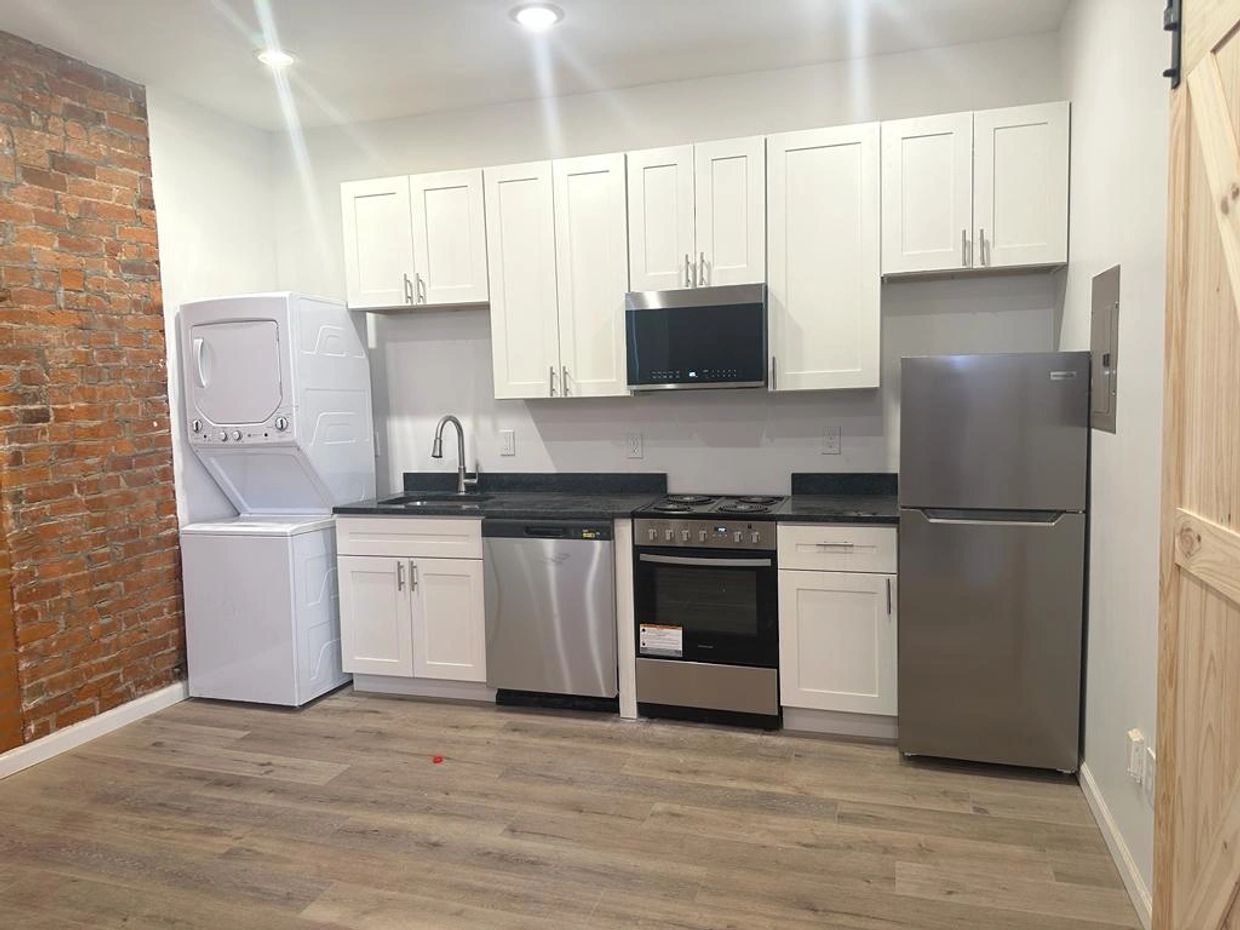 Modern kitchen with white cabinets, stainless steel appliances, and exposed brick wall.