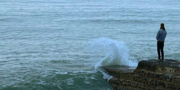 Person standing on rocks watching ocean waves crash.