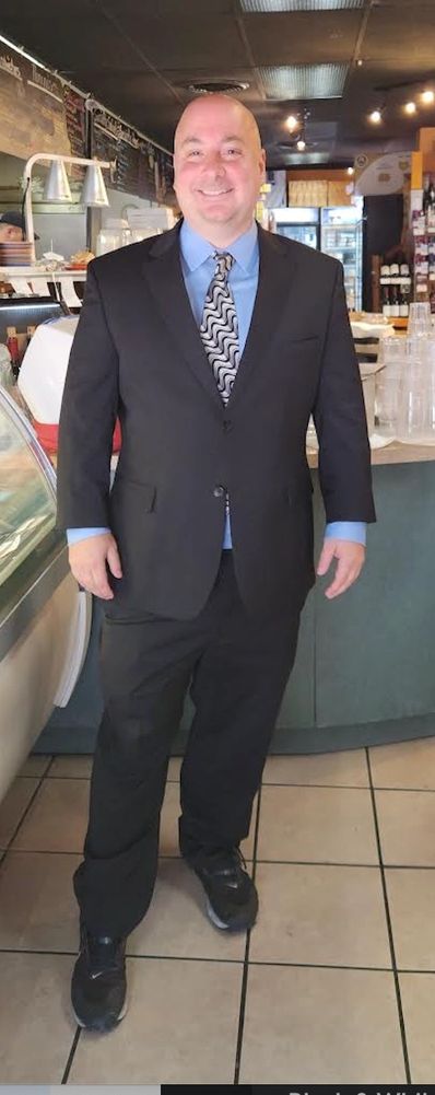 Man in a suit with a patterned tie and sneakers smiling indoors.