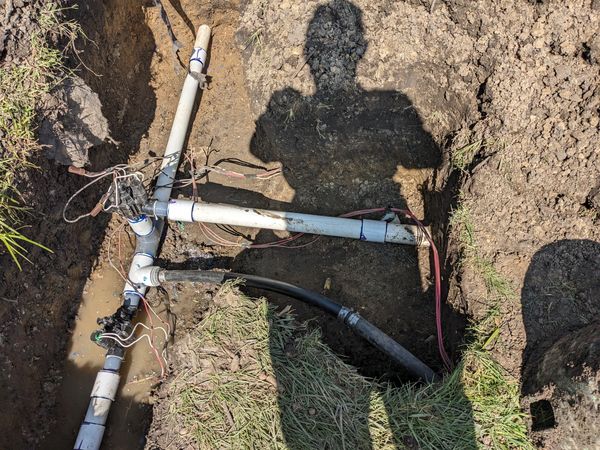 A man is standing in the dirt with two pipes.