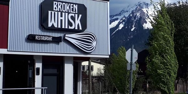 Sign for Broken Whisk restaurant with a mountain backdrop.