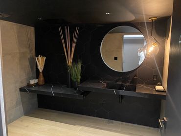 Modern bathroom with black hexagonal tiles and floating black marble sinks.