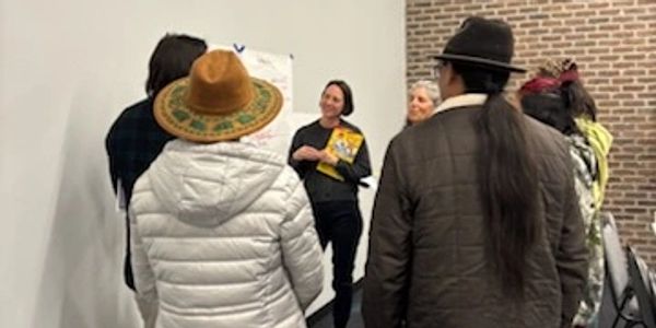 A group of people listening to a presenter holding a booklet indoors.