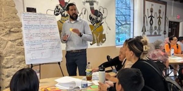 A man presenting to a group in a classroom setting with notes on a flip chart.