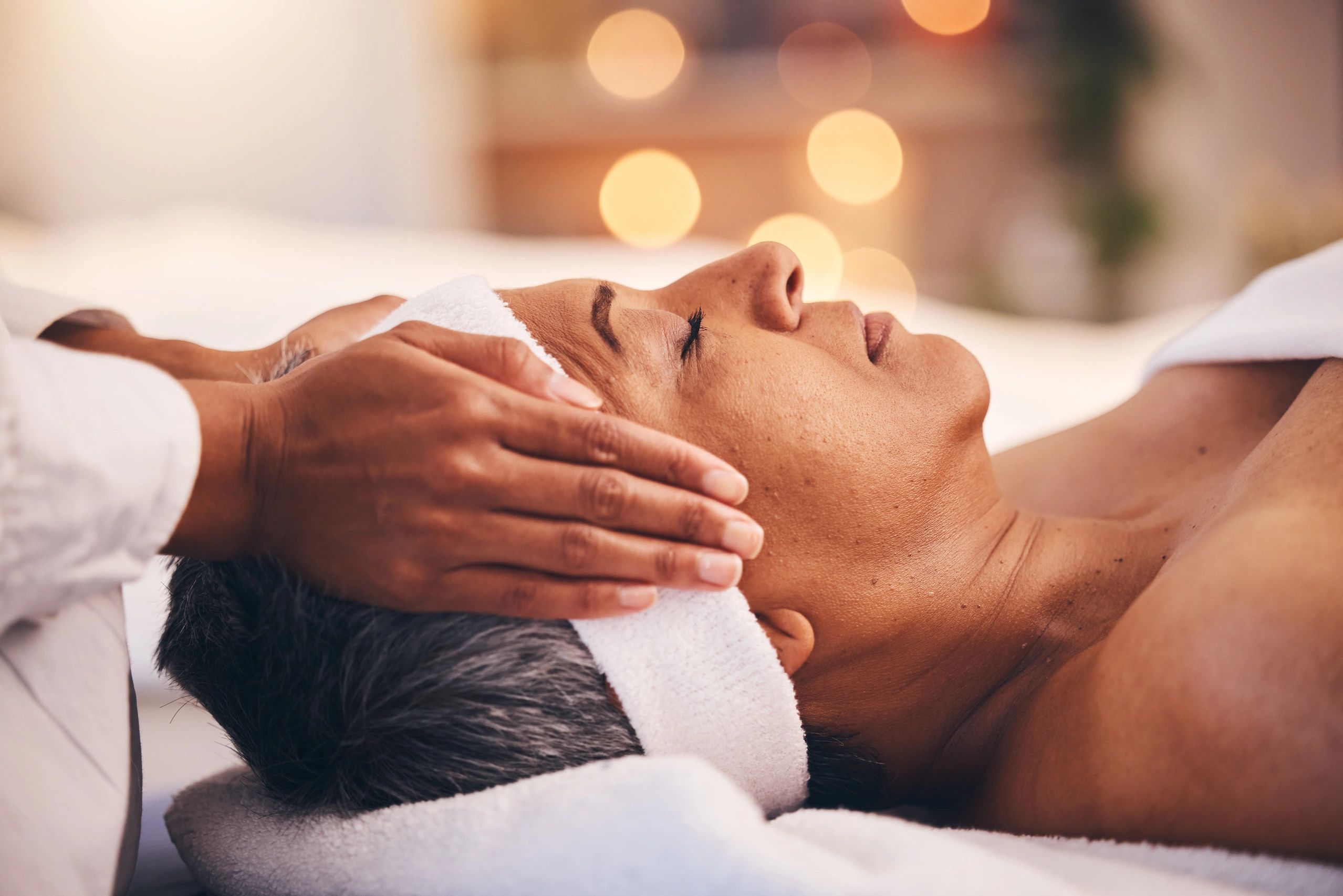 A woman receiving a relaxing head massage with a white towel around her head.