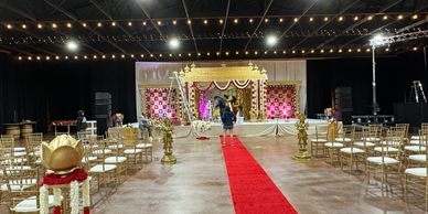 Indoor wedding setup with golden decorations and a red carpet aisle.