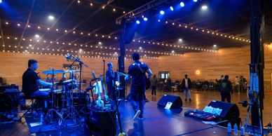 Band performing on stage in a spacious, dimly lit venue with string lights.