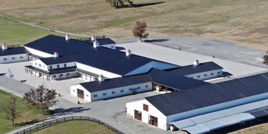 A large, modern barn complex with black roofs in a spacious rural field.