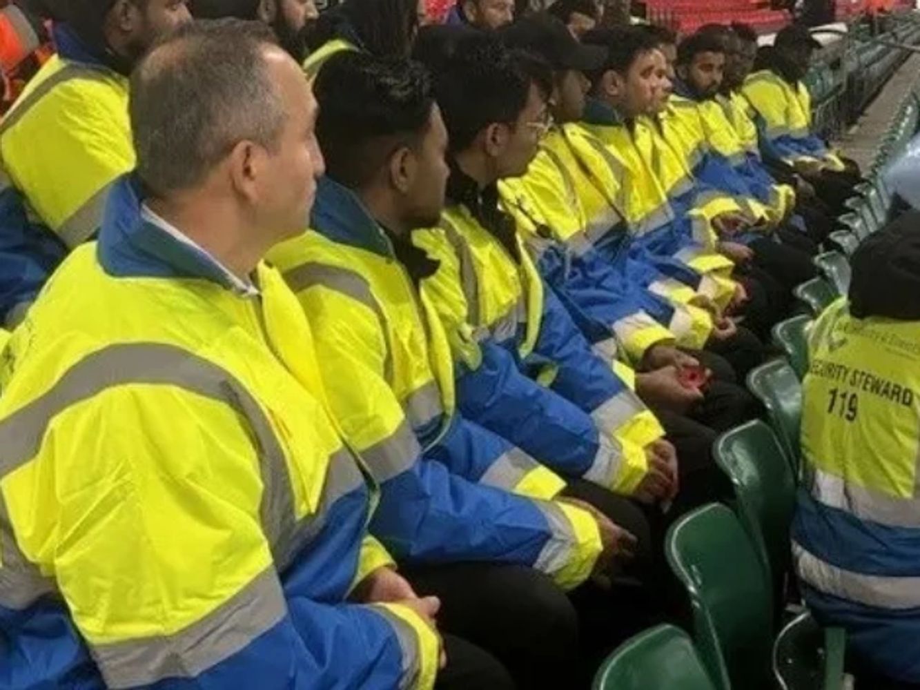 Group of event stewards in yellow and blue jackets sitting in a row.