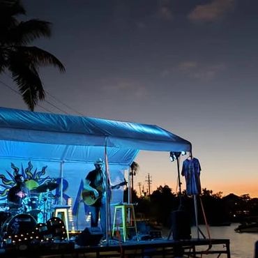 A band performs under blue lights at sunset near water.