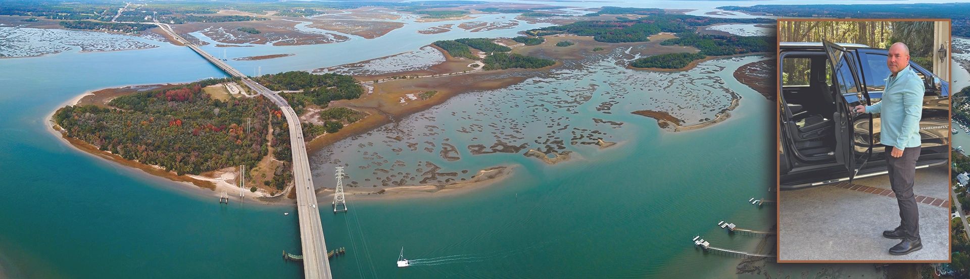 A man standing beside an open car door with a scenic coastal bridge in the background.
