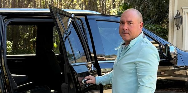 Man opening the door of a black Chevrolet Suburban outside a house.