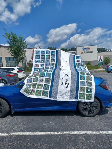A colorful music-themed quilt draped over a blue car.