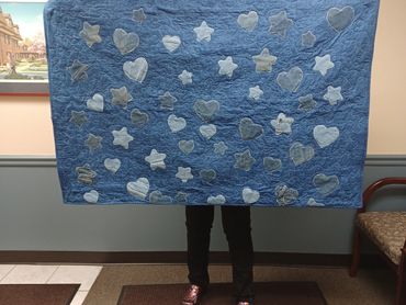 Person holding a blue quilt with star and heart shapes.