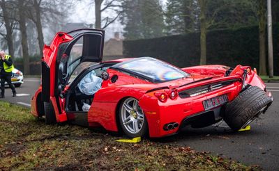 Red sports car with severe rear damage and detached wheels at accident scene.