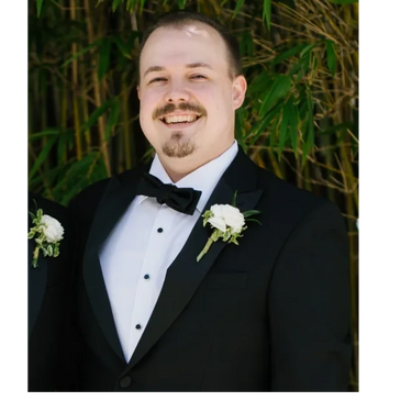 A smiling man in a tuxedo with a white boutonniere.