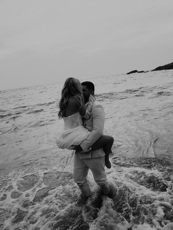 Couple embracing in the ocean waves in black and white.