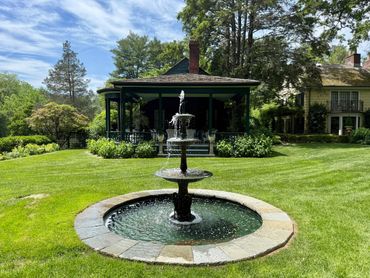 Elegant backyard fountain in front of a cozy porch surrounded by greenery.