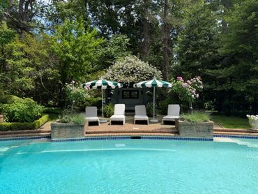 A serene backyard pool area with loungers and umbrellas surrounded by lush greenery.