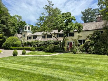 Elegant large house with manicured lawn and lush greenery on a sunny day.