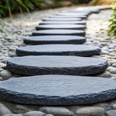 This image shows a garden path made of oval, dark gray stepping stones laid over a bed of small