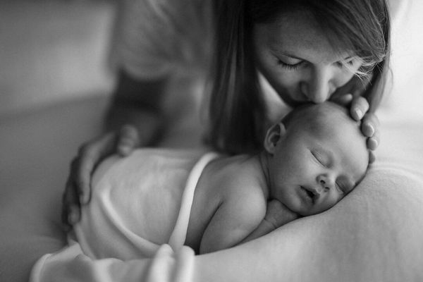 mamma accarezza e bacia il suo bimbo addormentato a pancia in giu per servizio fotografico neonato