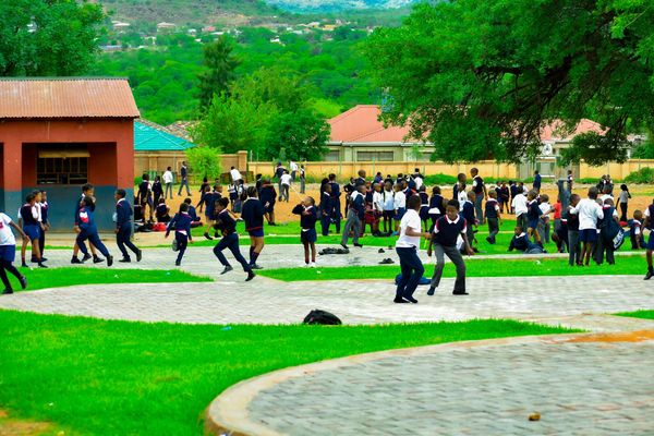 Students in uniform play and gather in a schoolyard surrounded by greenery and buildings.