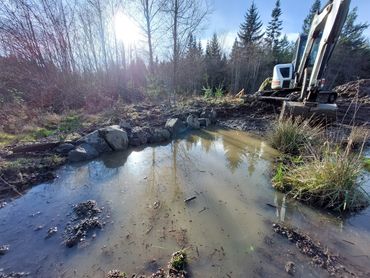 Water detention basin full of water with rocks and rushes and excavator on a sunny day