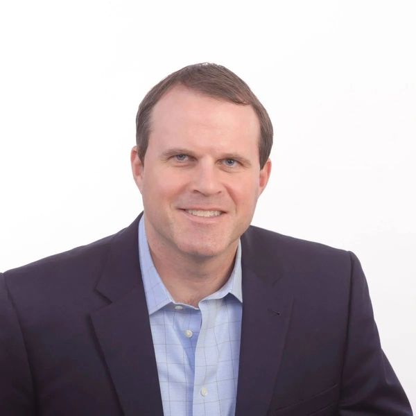 Smiling man in business attire with a plain white background.