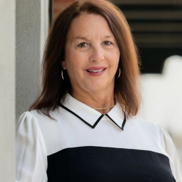 Smiling woman with long brown hair wearing a black and white blouse.