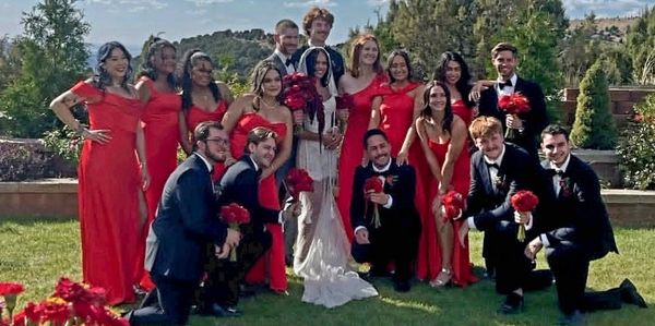 A wedding party with bridesmaids in red and groomsmen in black suits.