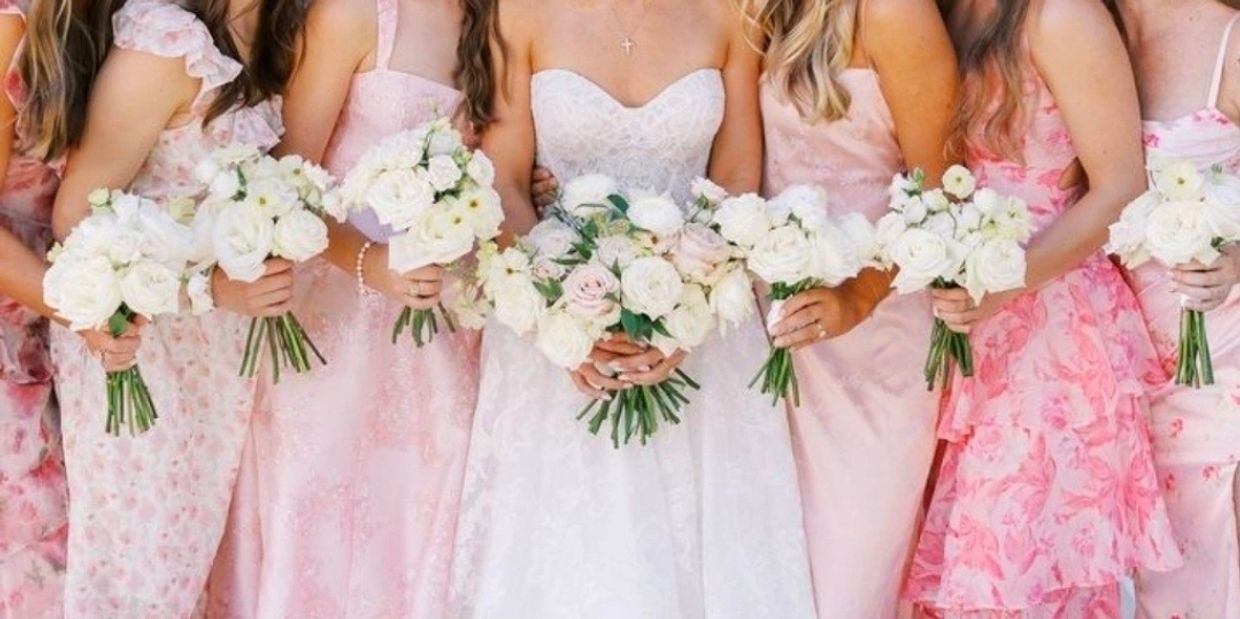Bridal party in pastel pink dresses holding white bouquets.