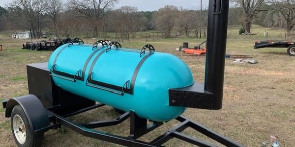 Blue barrel smoker on a trailer in a field.