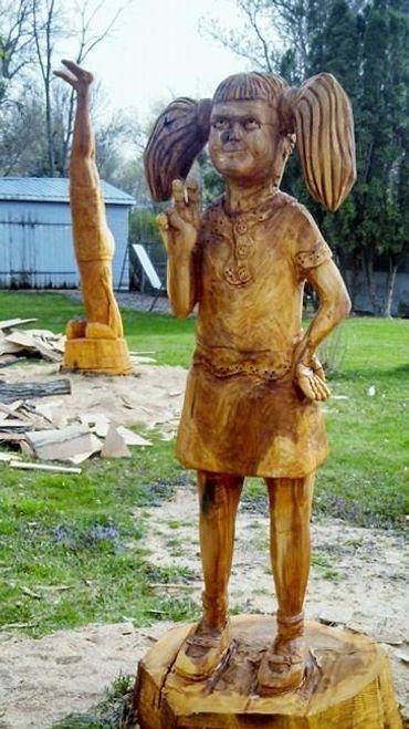 chainsaw carved little girl with peace sign and man in shoulder stand