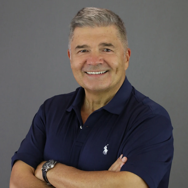 Smiling middle-aged man with gray hair wearing a navy polo shirt.