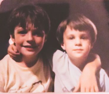Two young boys smiling with arms around each other in a warm, nostalgic photo.