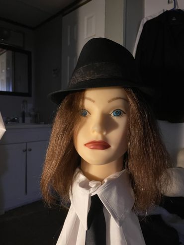 Mannequin head with brown hair, hat, white shirt, and black tie.