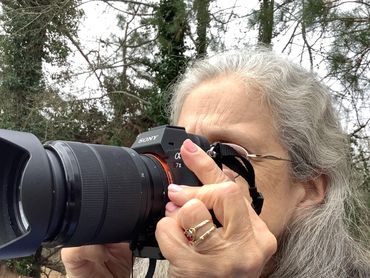 Woman with gray hair taking a photo with a Sony camera outdoors.