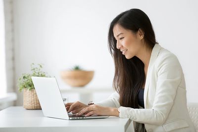 A woman in a white blazer using a laptop and smiling.