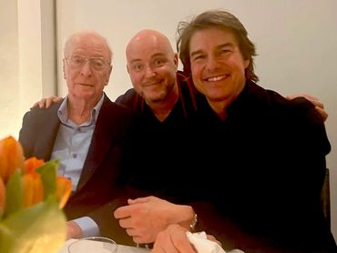 Three men posing closely together, smiling warmly at the camera indoors.