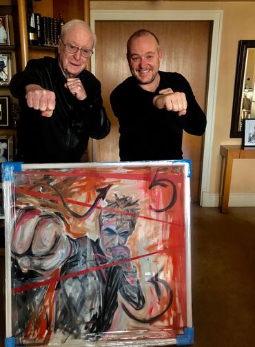 Two men posing with fists extended behind a painting of a fist and a man.