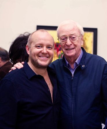 Two men smiling and posing together indoors, one older and one younger.