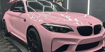 A sleek pink BMW car with black rims in a showroom.